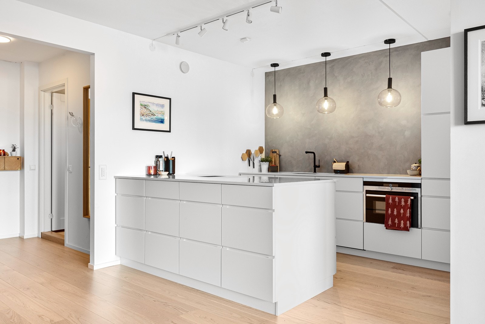 Kjøkken og stue i en sosial og moderne, åpen løsning med kjøkkenøy som et naturlig skille mellom sonene. Galleribilde