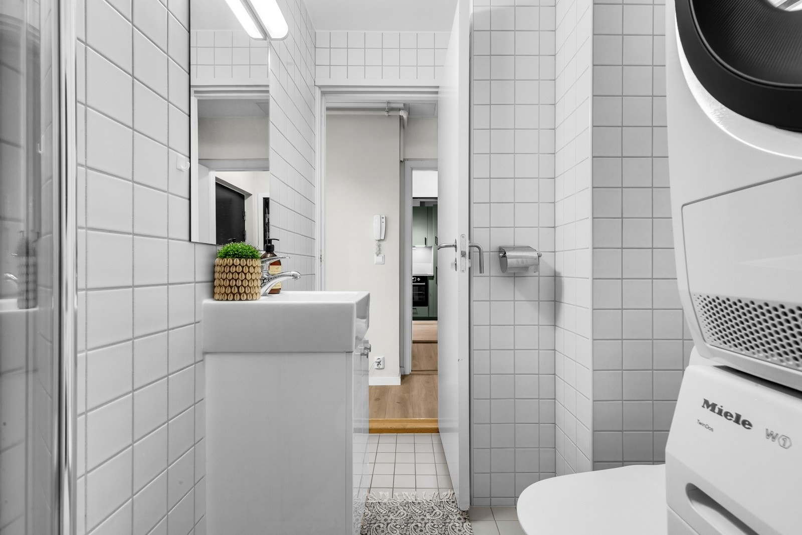 Baderommet inneholder servant med underskap, speil med belysning og stikkontakt, dusjhjørne med innfellbare glassdører og toalett. Galleribilde