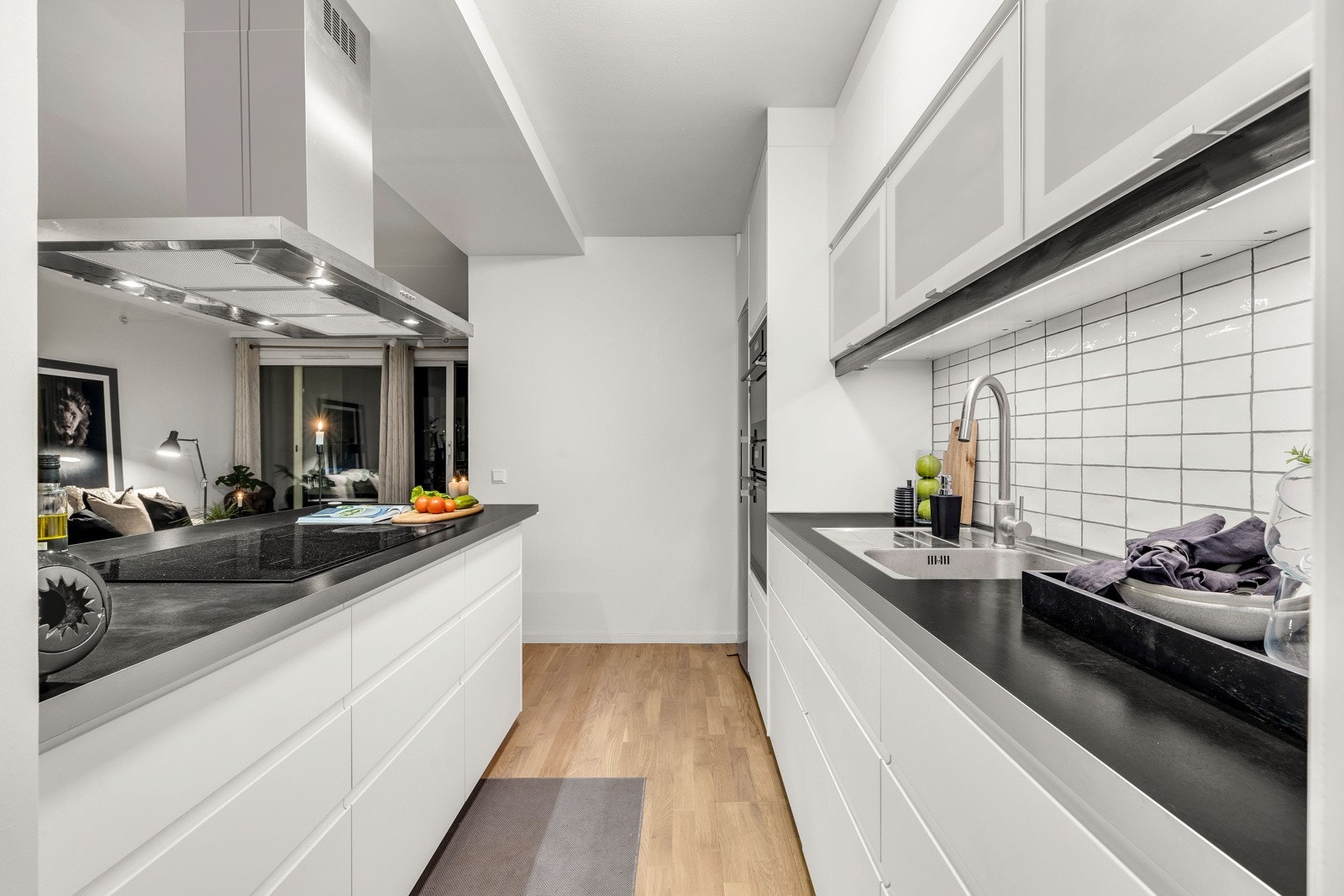 Det er godt med skap- og benkeplass på kjøkkenet. Over benken er det belysning og hvite fliser, og over kokesonen er det montert en takhengt ventilator i børstet stål. Av hvitevarer har kjøkkenet integrert induksjonstopp, stekeovn, oppvaskmaskin og mikro Galleribilde