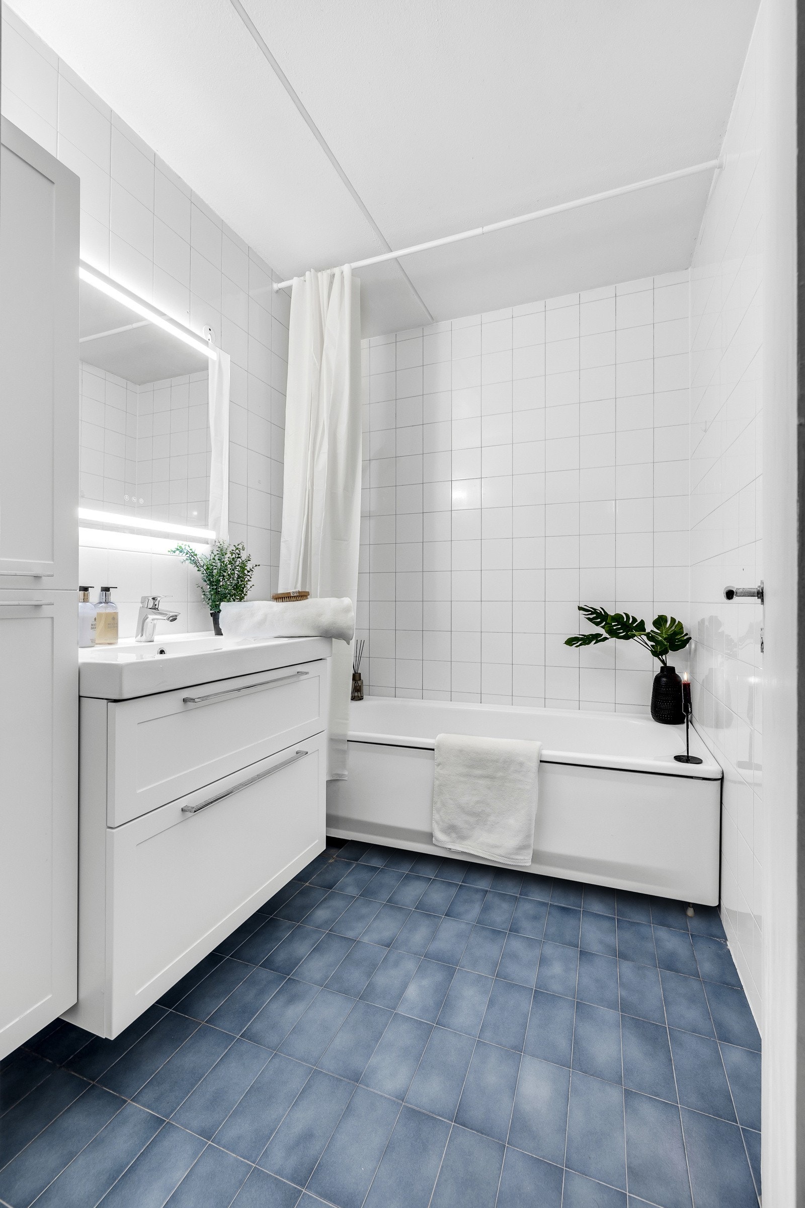 På badet er det hvite veggfliser og blå gulvfliser med varme. Galleribilde