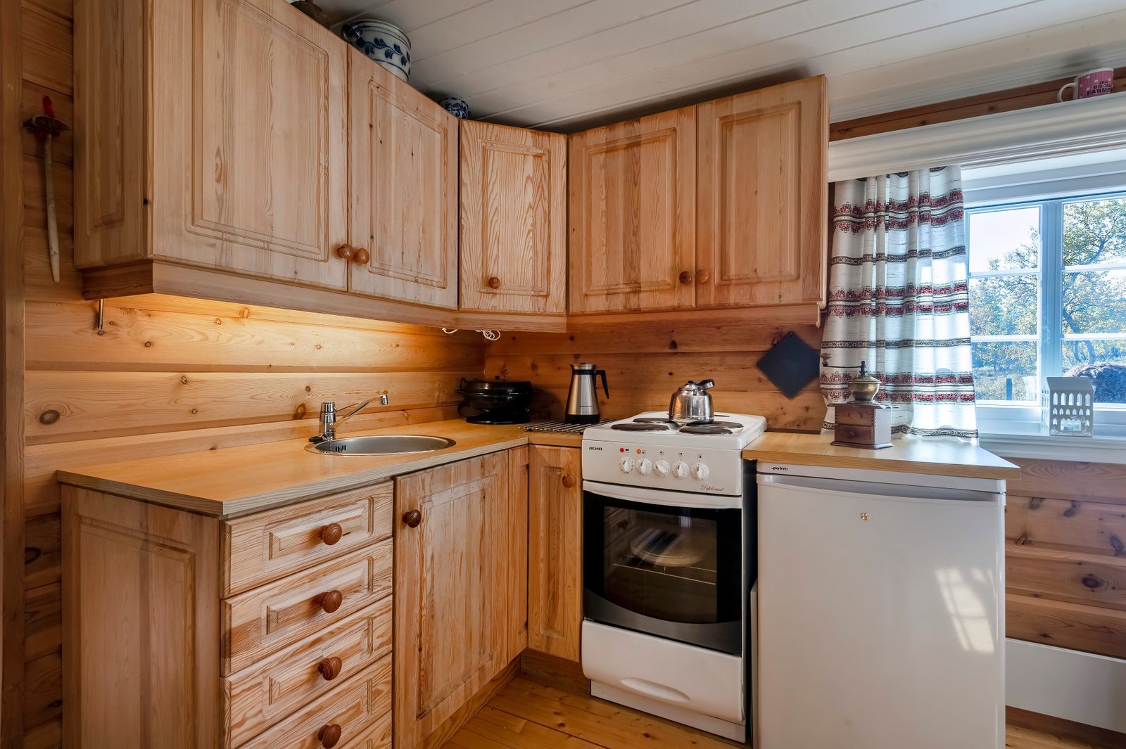 Kjøkkeninnredning med over- og underskap, fronter i
heltre, laminerte benkeplater og kjøkkenvask. Galleribilde