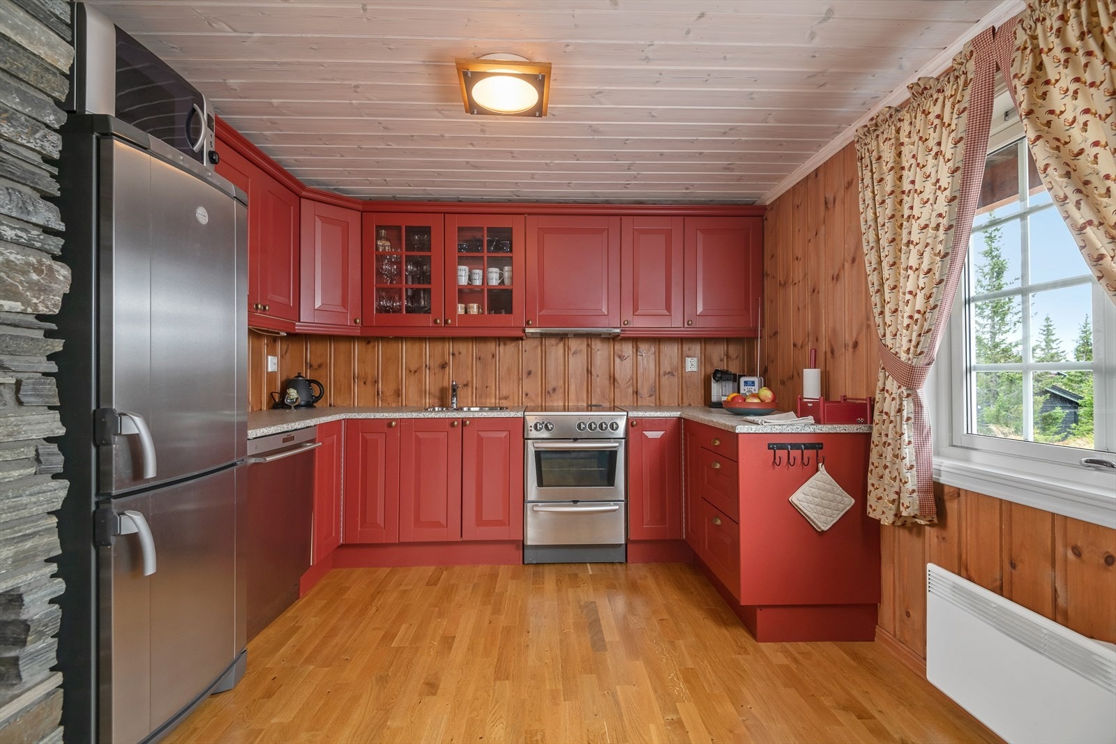 Kjøkken i rødmalt farge med plass til oppvaskmaskin, kjøleskap og komfyr. Galleribilde