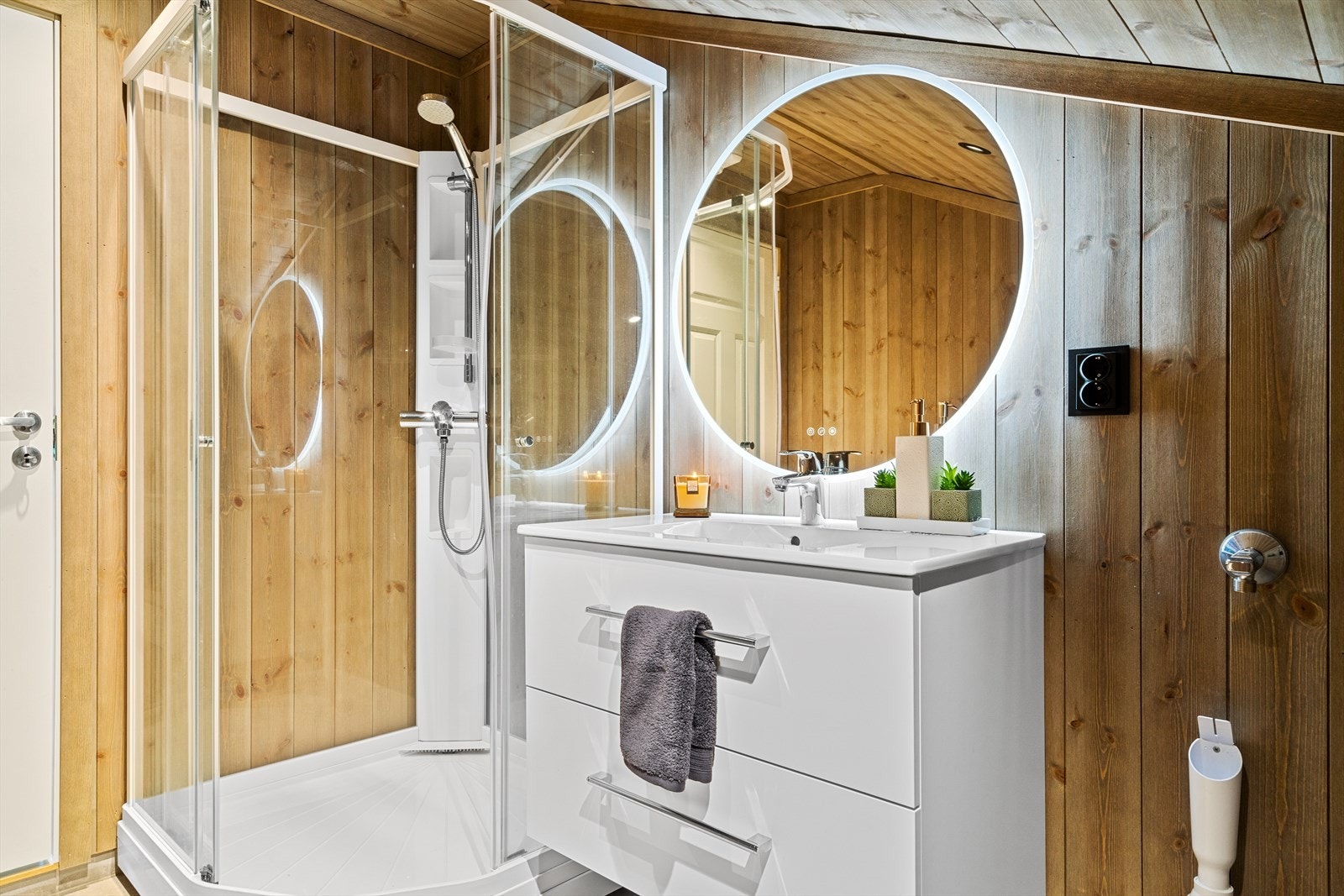 Her er det innredet med helstøpt servant på skuffeinnredning, speil med integrert belysning, dusjkabinett, vegghengt toalett, og opplegg for vaskemaskin. Galleribilde