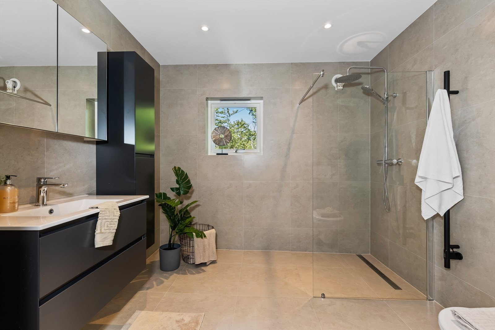 Delikat og innbydende baderom fra 2022 med store fliser på gulv og vegger samt malte takflater med downlights i himling. Galleribilde