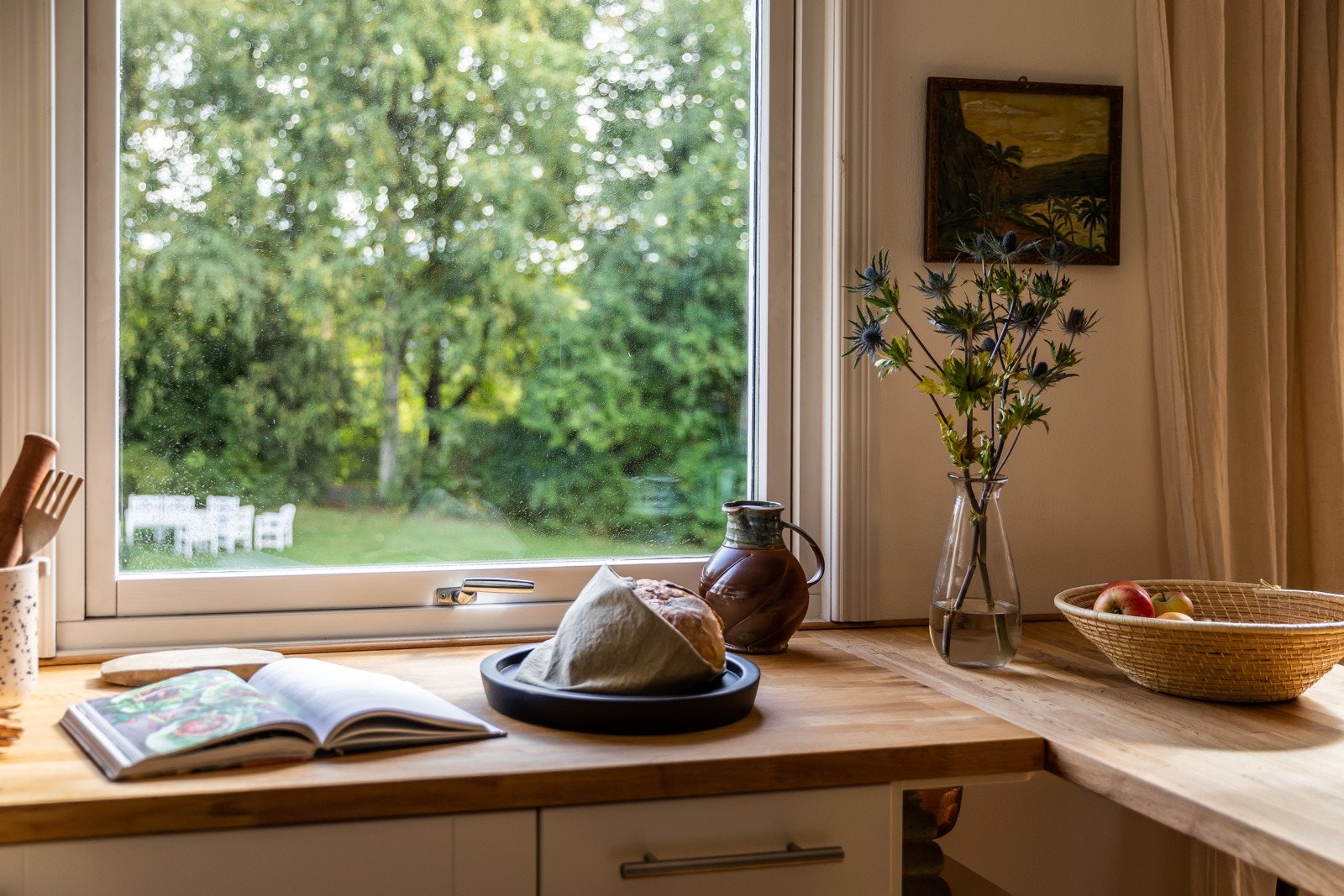 Et stort vindu over kjøkkenbenken gir grønn utsikt til parkmessig hageareal. Galleribilde