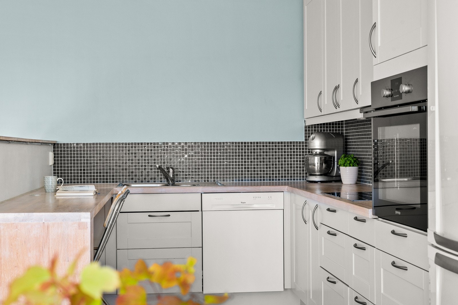 Kjøkkeninnredning med lyse profilerte fronter, heltre benkeplater, dobbel oppvaskkum og mosaikkfliser mellom over- og underskap. Galleribilde