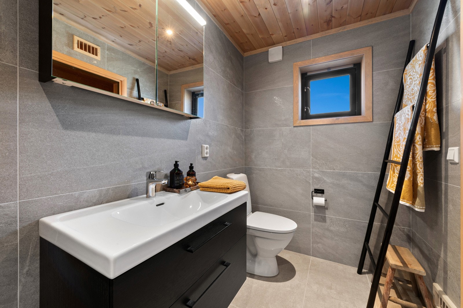 Badet har store, grå fliser på gulv og vegger, samt gulvvarme og downlights. Galleribilde