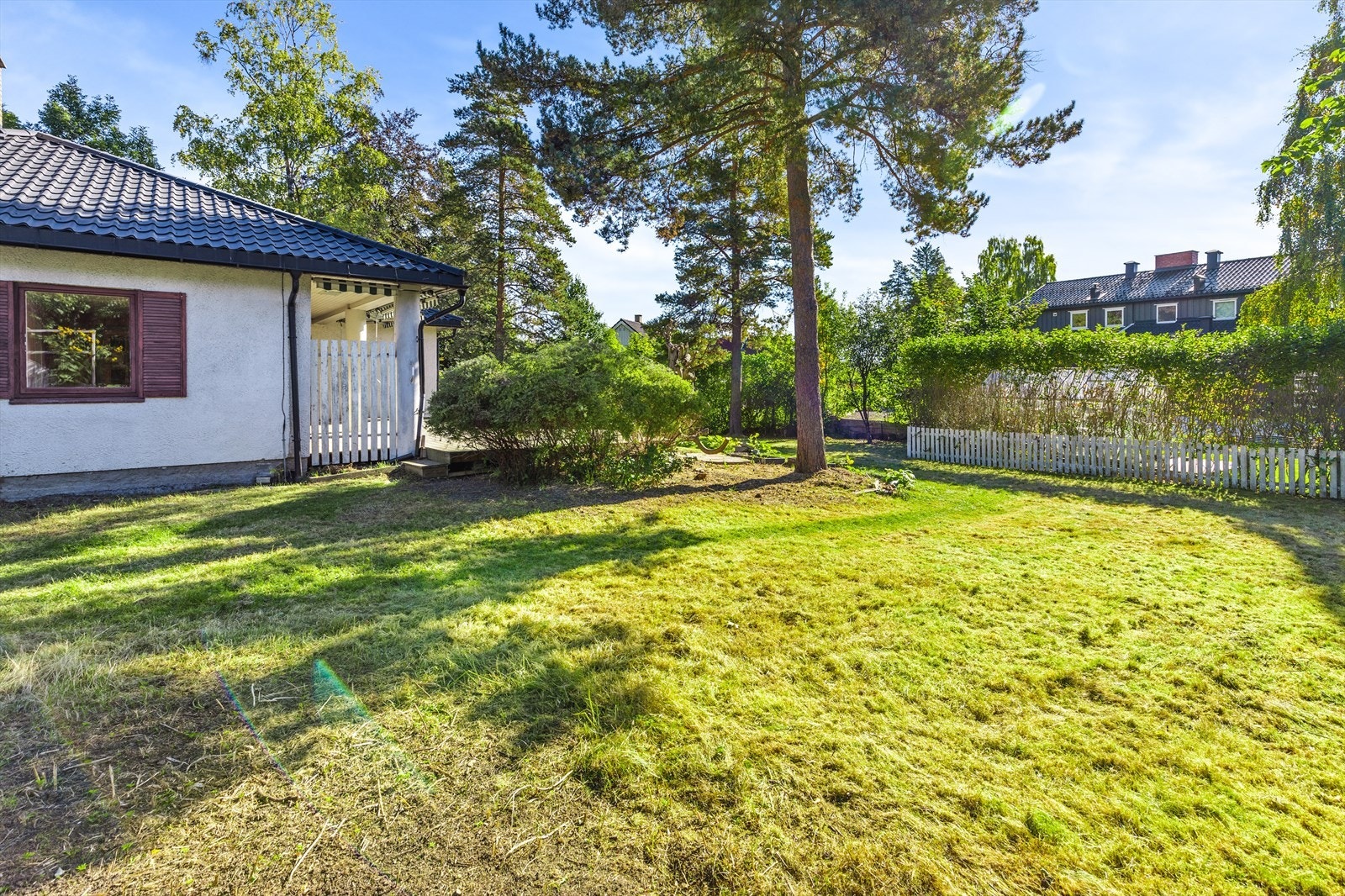 Stor tomt som er opparbeidet med plen, busker og trær. Det er satt opp gjerde rundt tomten Galleribilde