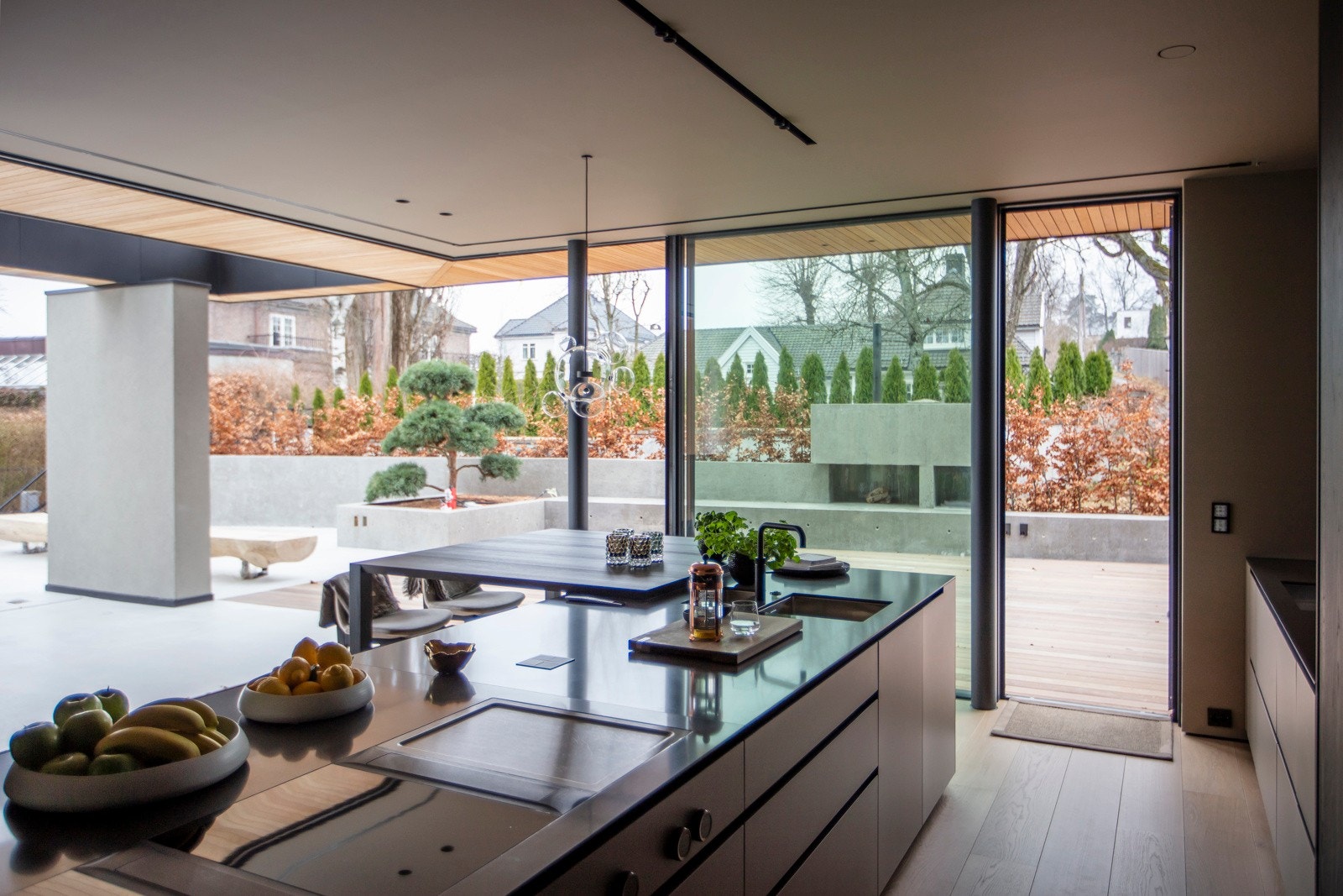 De høye pocketdørene gjør det mulig å lukke for et rent og moderne uttrykk hvor gjestene kan samle seg rundt øyen med lekker peis og med utsikt til bassengområdet. Galleribilde