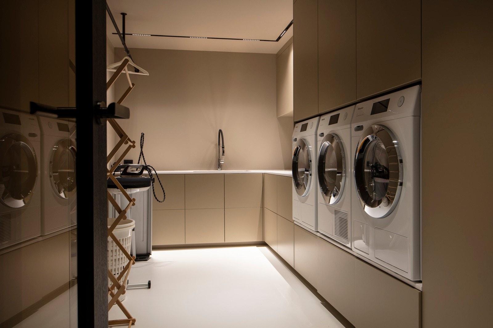 I kjelleretasjen ligger det et pent og meget praktisk innredet vaskerom med sandfargede vegger og matchende, innholdsrik skapinnredning. Det er nedfelt kum i en hvit benkeplate i corian, og opplegg for vaskemaskiner og tørketrommel. Galleribilde