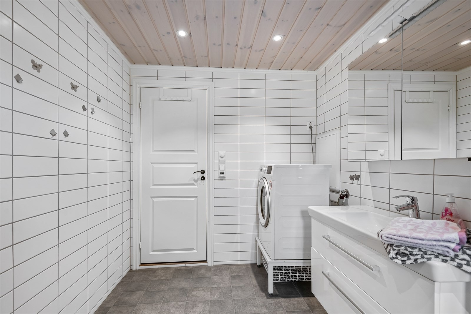 Dusjhjørne med innfellbare glassdører, servantinnredning og opplegg for vaskemaskin. Galleribilde