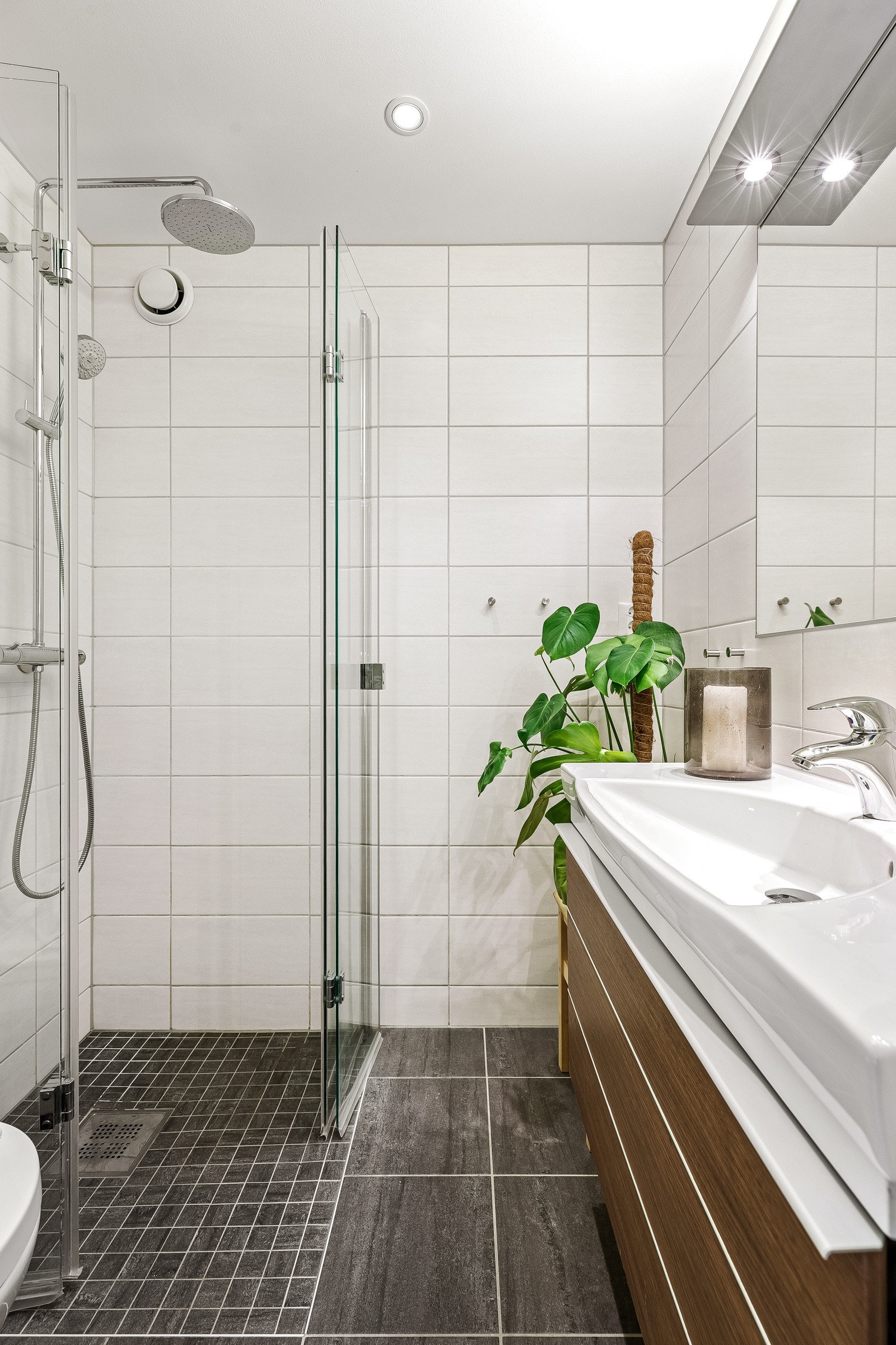Badet inneholder vegghengt toalett, benkeskap med servant, dusjdører i glass og opplegg til vaskemaskin. Galleribilde
