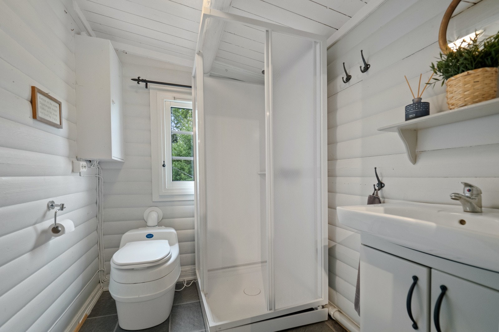 Vegghengt servantskap med skapdører, dusjkabinett med skyvedører og gulvstående seperasjonstoalett Galleribilde