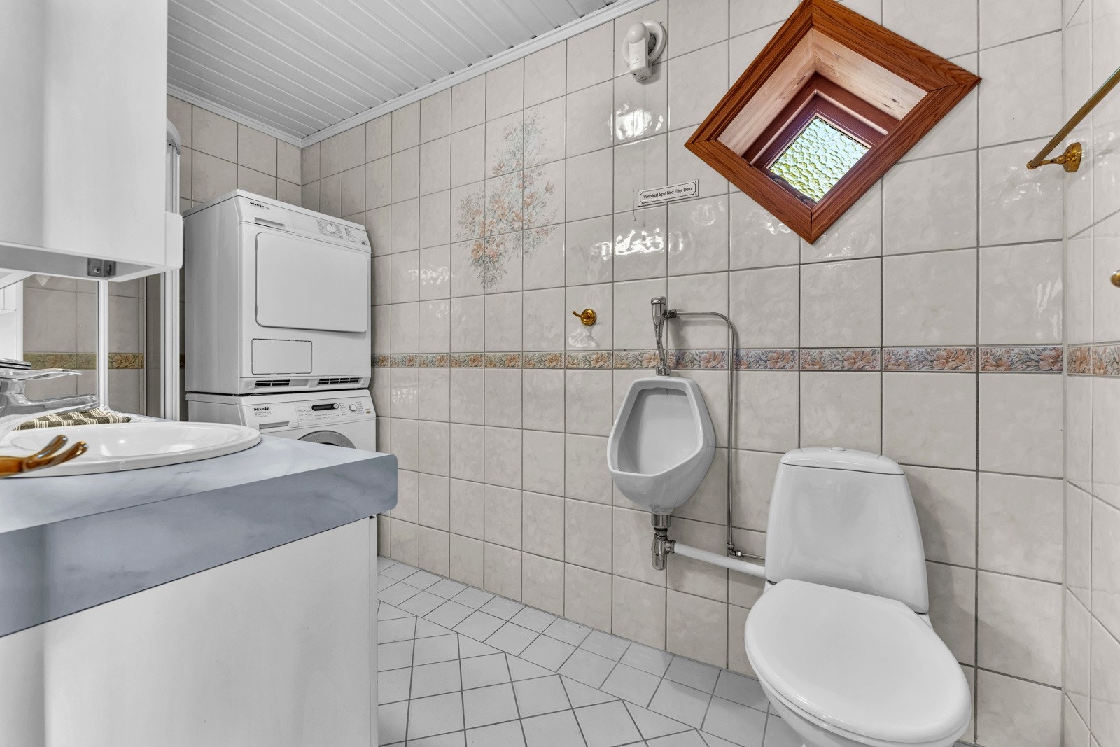 Badet i eneboligen har flislagte overflater, gulvvarme og opplegg for vaskesøyle. Galleribilde