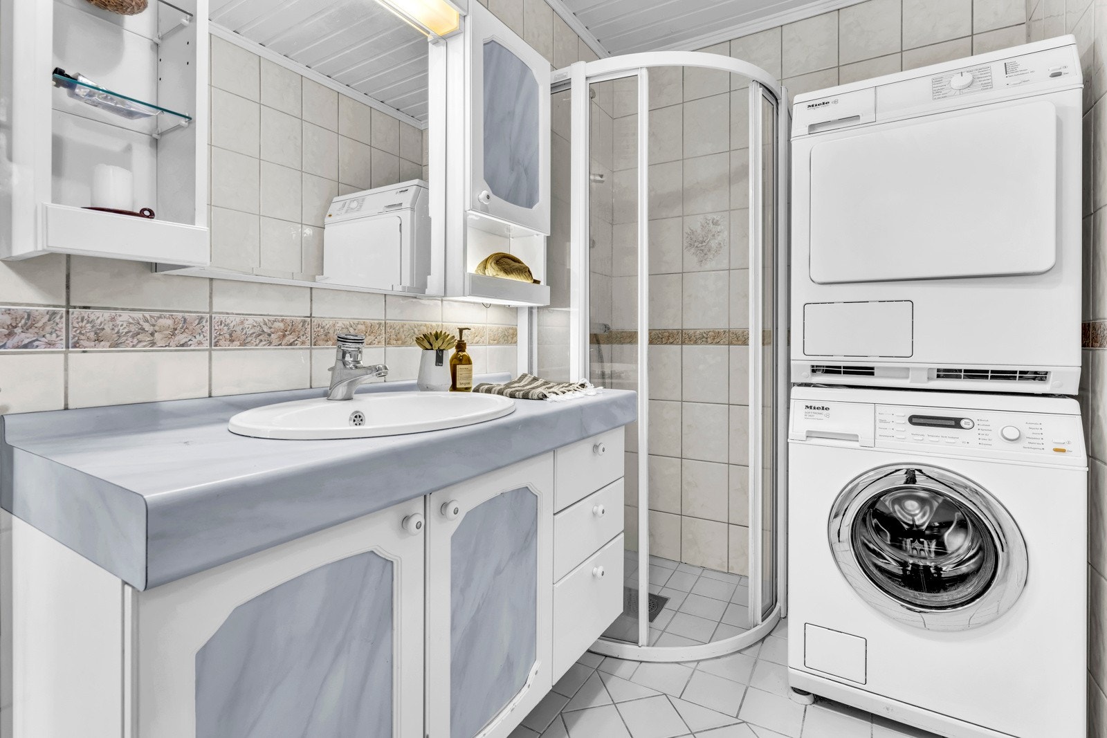 Badet har dusjhjørne med skyvedører og hvit innredning med speil og veggskap. Galleribilde