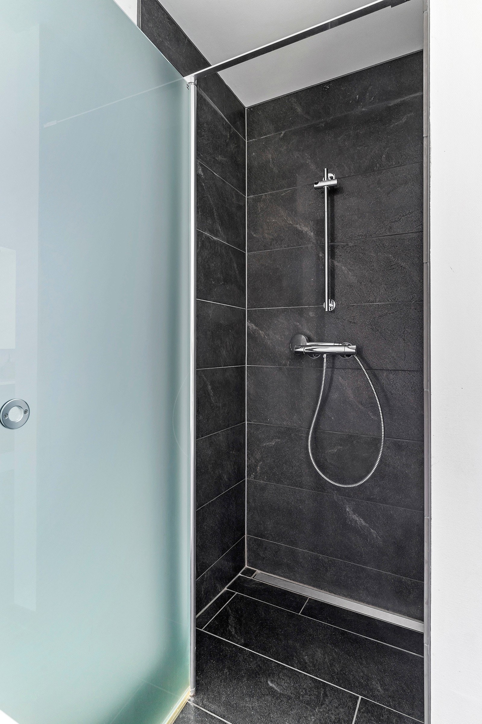 Dusjen har sorte fliser på gulv og vegg, samt frostet glassdør Galleribilde