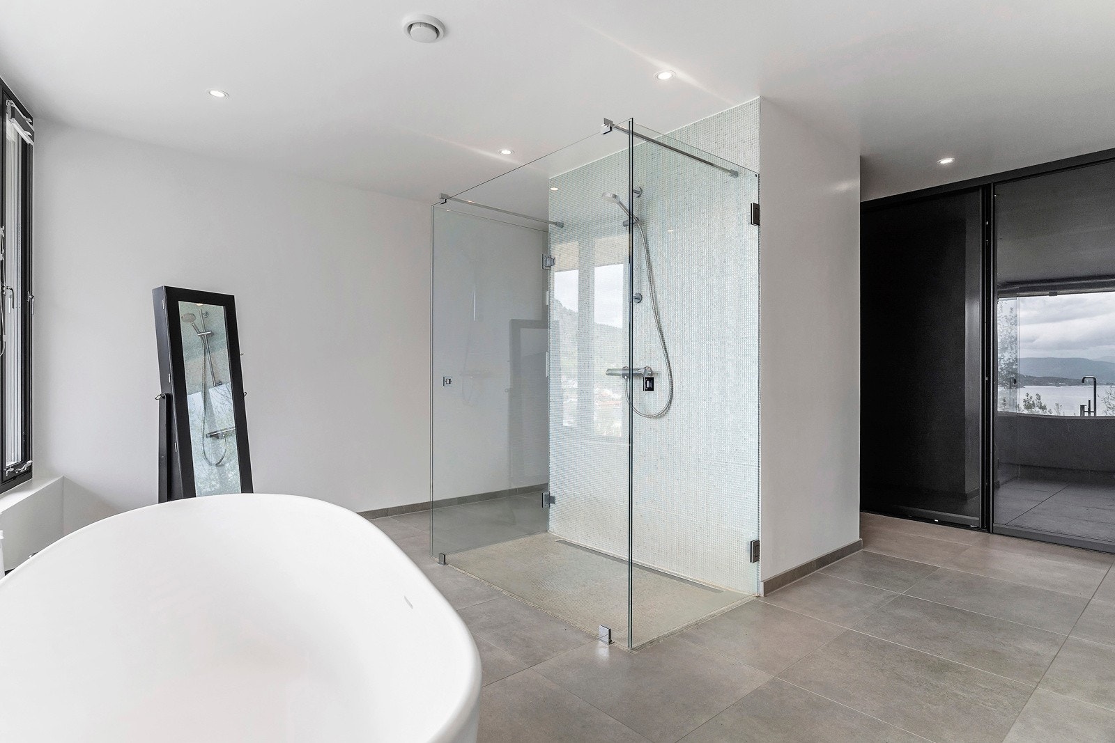 Badet er meget romslig med store grå fliser på gulv og en vegg med bare betong Galleribilde