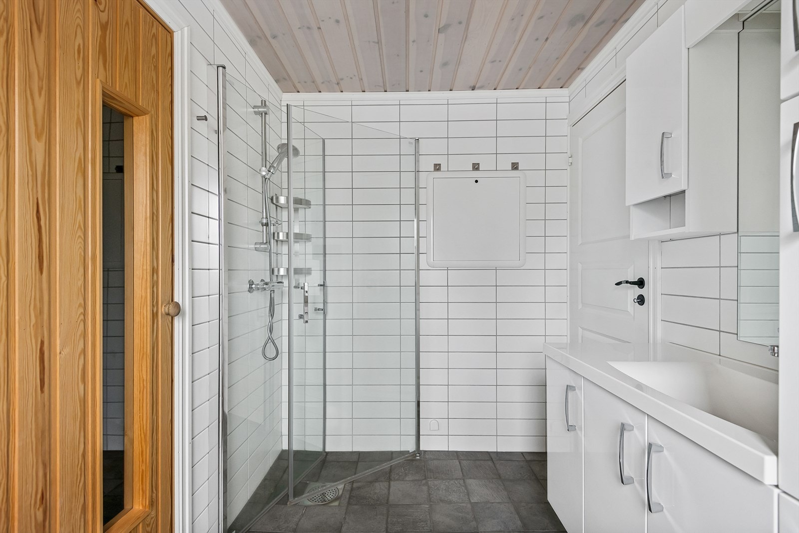 Lyst og stilrent bad/wc med flislagt dusjhjørne som har innfellbare dusjvegger i glass. Galleribilde