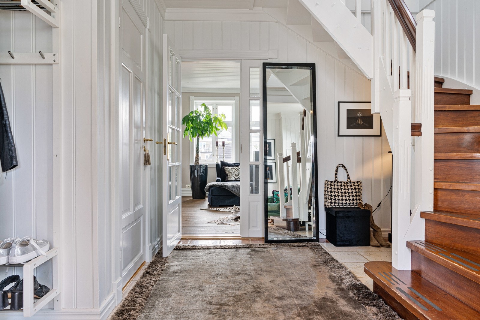 En stor fin hall med inngang til kjøkken, stue og en iøynefallende trapp opp til andre etasje. Galleribilde