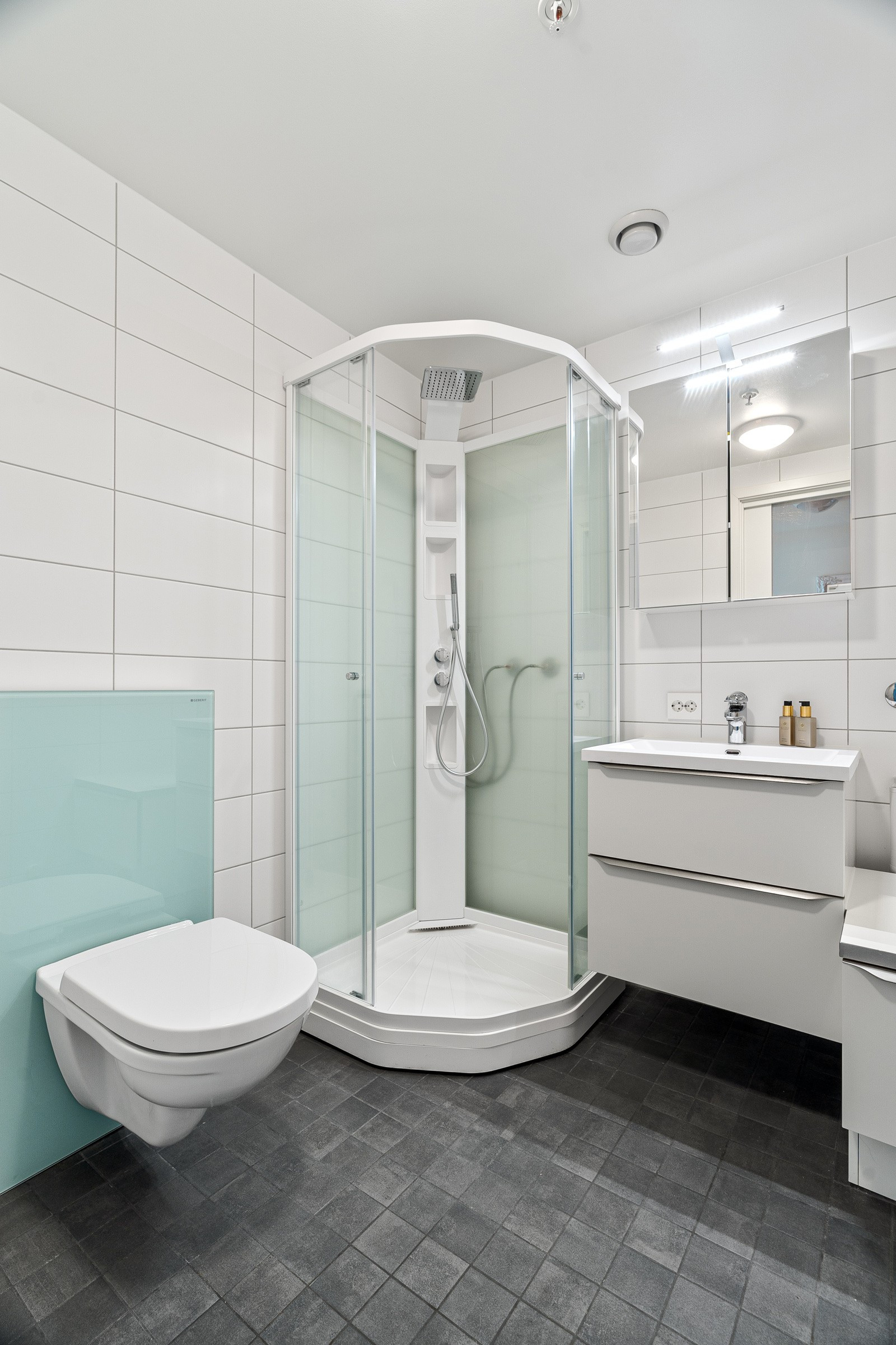 Badet er komplett flislagt med gulvvarme, innredning med nedfelt servant, veggmontert toalett, dusjkabinett og opplegg for vaskemaskin.
