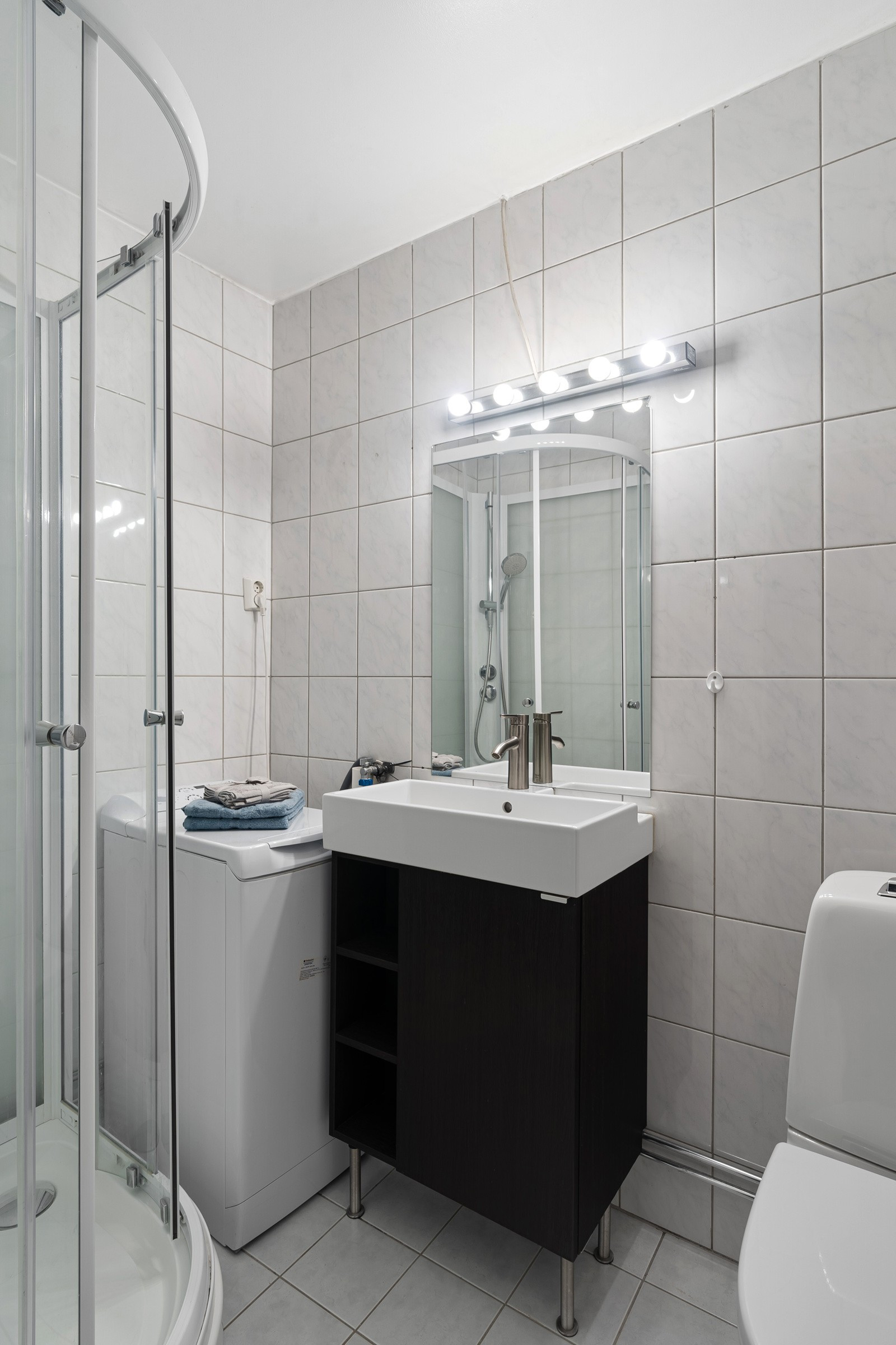 Badet er flislagt og innredet med servant, dusjkabinett, toalett og opplegg for vaskemaskin.