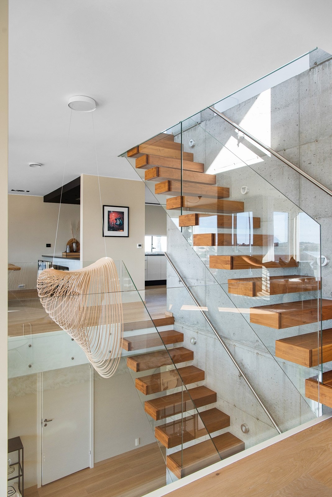 Trapperom / atrium med glassrekkverk rundt. Se også den stilige lysekronen som følger med. Denne er kuttet tynt ut med laser, av ett stykke bjørkefiner. Designlampen er fra Luceplan og heter Illian. Galleribilde