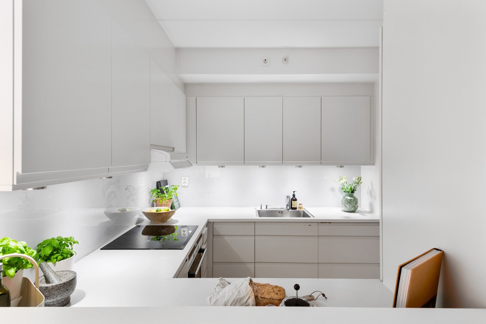 HTH kjøkkeninnredning med hvite matte fronter, benkeplater i laminat, underlimt oppvaskkum, ventilator og integrerte hvitevarer. Galleribilde