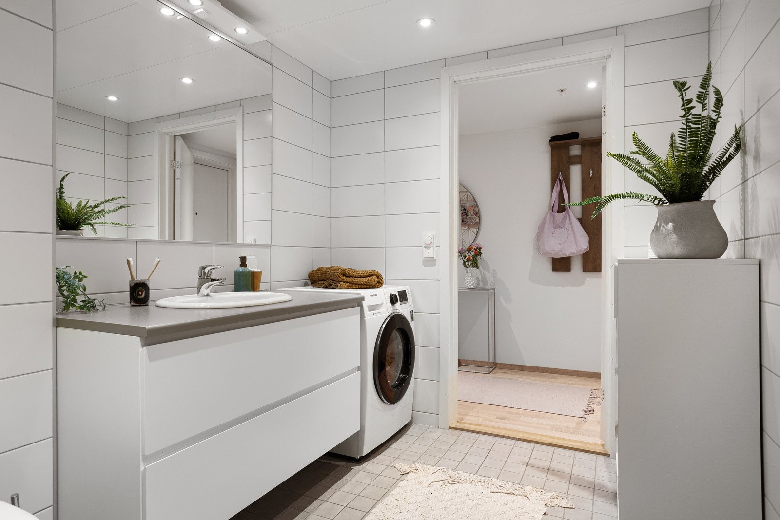 Delikat baderom utstyrt med benkeskap, speil og belysning over servant, dusj med innfellbare dører i herdet glass, servant og veggfestet klosett. Galleribilde