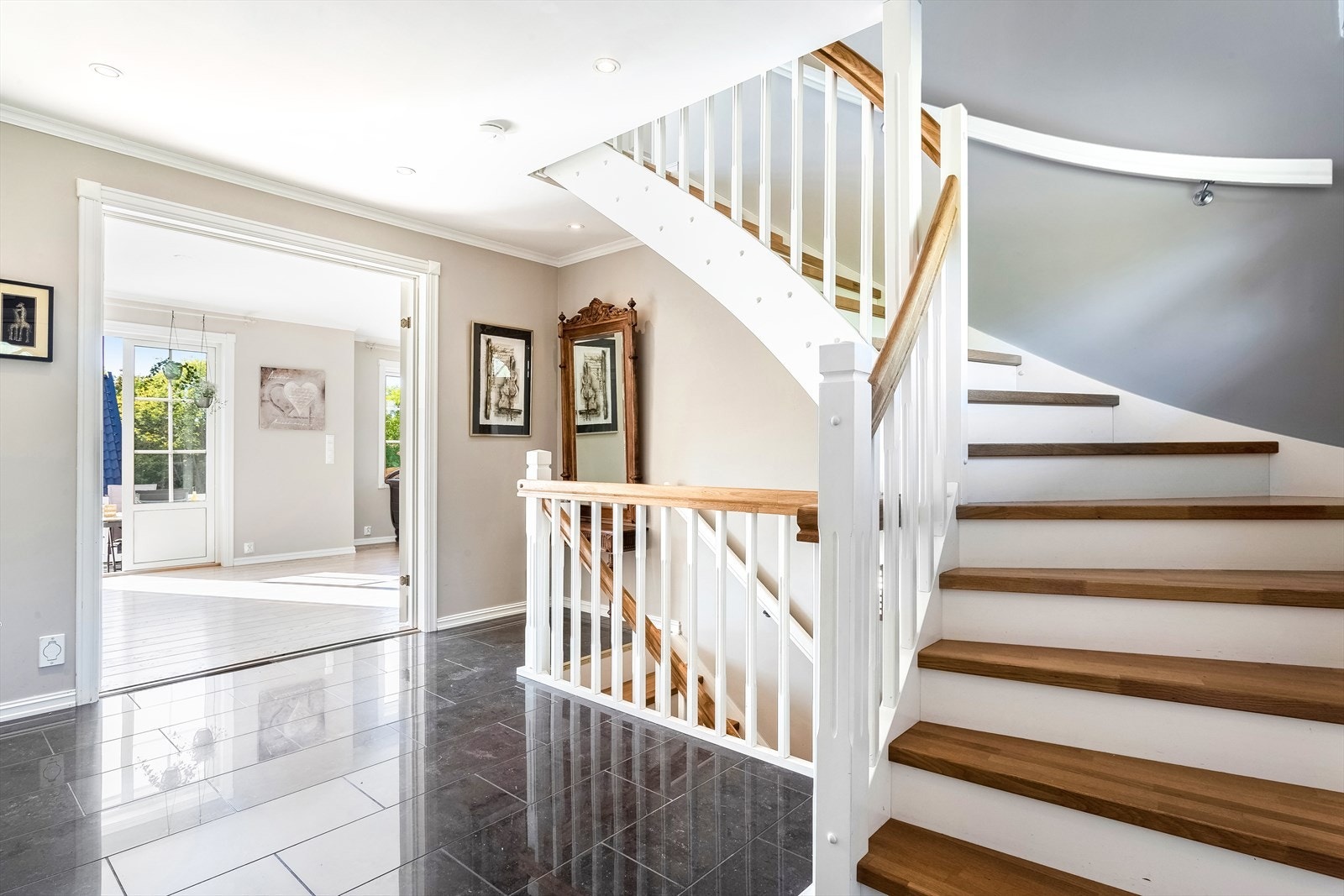 Stor og innbydende hall med flislagt gulv og flott trapp med eiketrinn opp til 2.etasje og ned til u.etasje Galleribilde