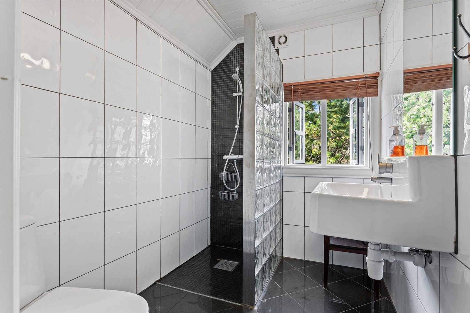 Badet er helfliset og inneholder servant, toalett og dusj med glassbyggerstein. Galleribilde