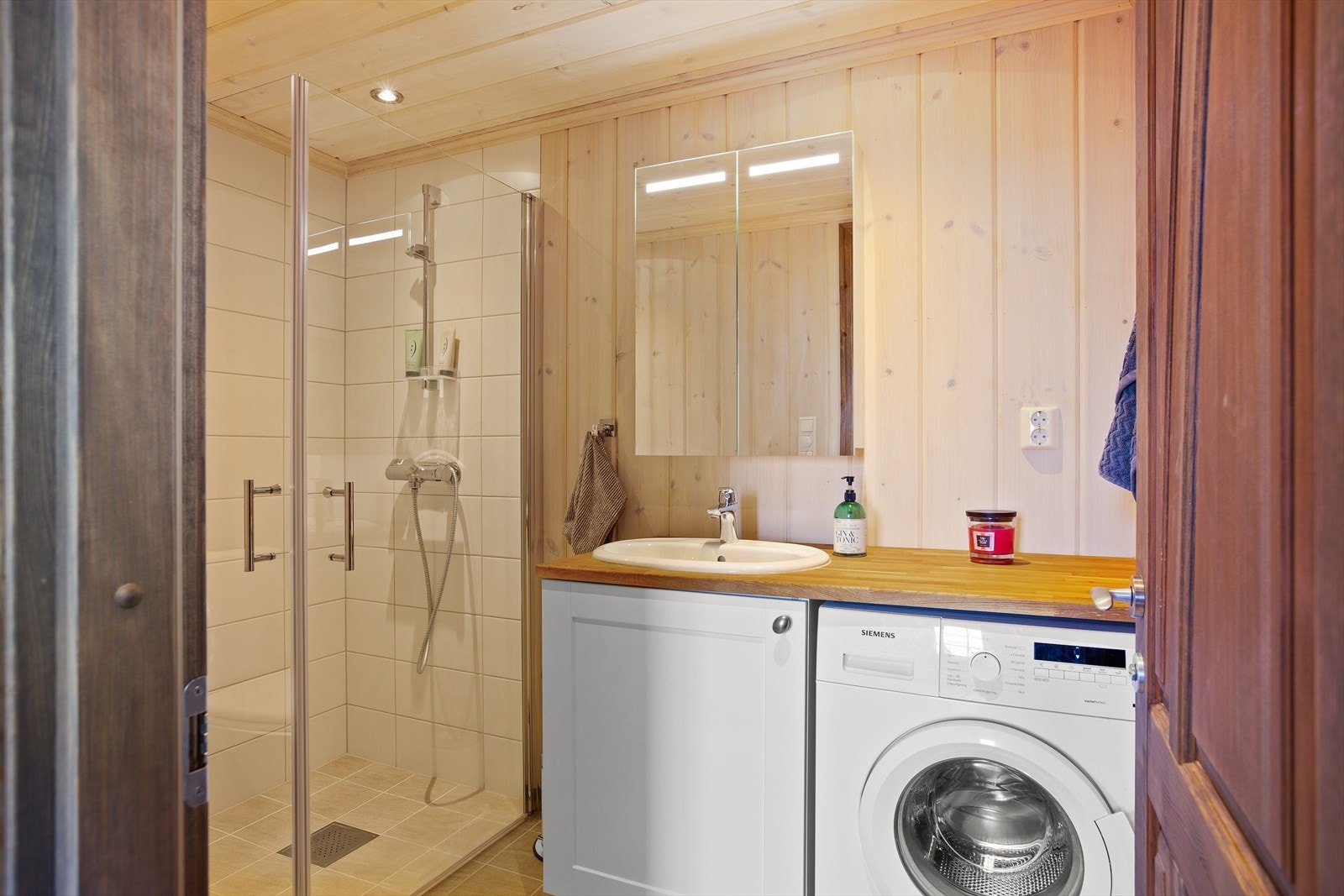 Pent baderom som inneholder gulvstående toalett, servant med underskap, dusj med dusjvegger og opplegg for vaskemaskin. Galleribilde