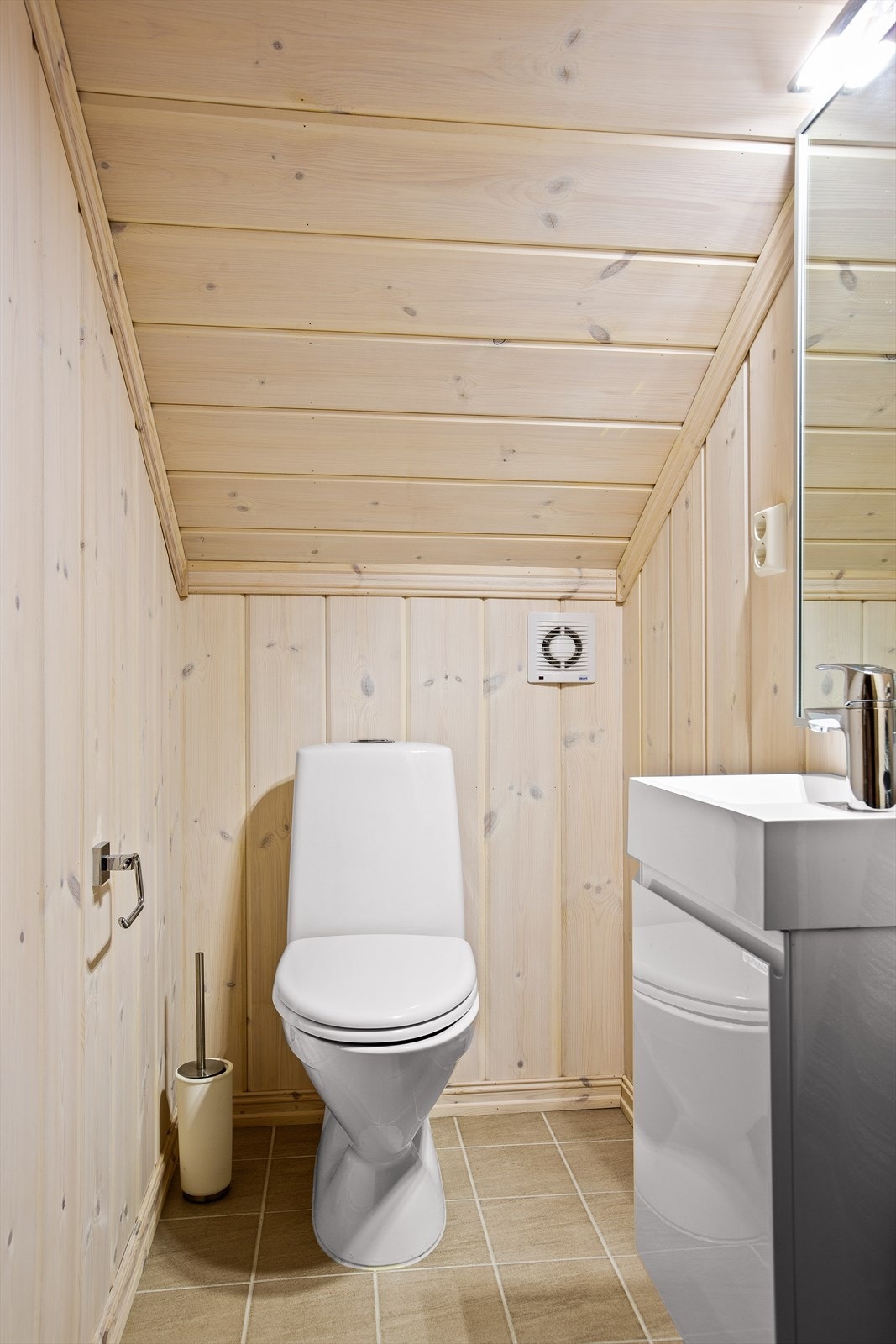 Toalettrommet står i stil med baderommet med fliser på gulv, panel på vegger og i himling. Servant med underskap, speil og gulvmontert toalett. Varme i gulv. Galleribilde