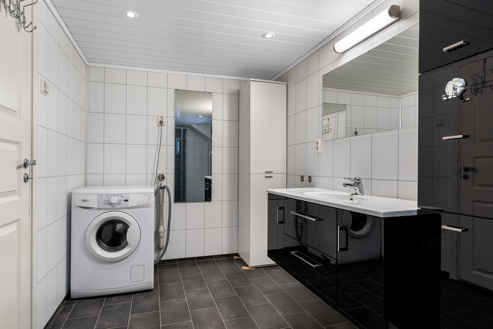 Badet har stort servantskap, dusjhjørne med dører, vegghengt toalett og opplegg for vaskemaskin. Mekanisk avtrekk med ventil i vegg. Galleribilde