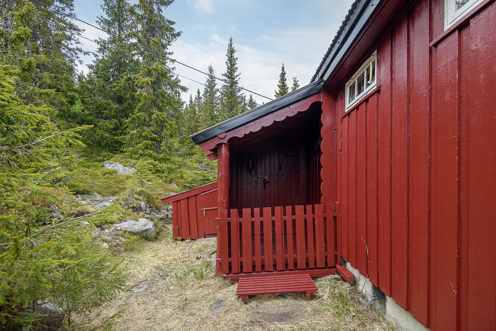 Hytta har et overbygget inngangsparti. Til venstre i bilde er det en utvendig bod. Galleribilde