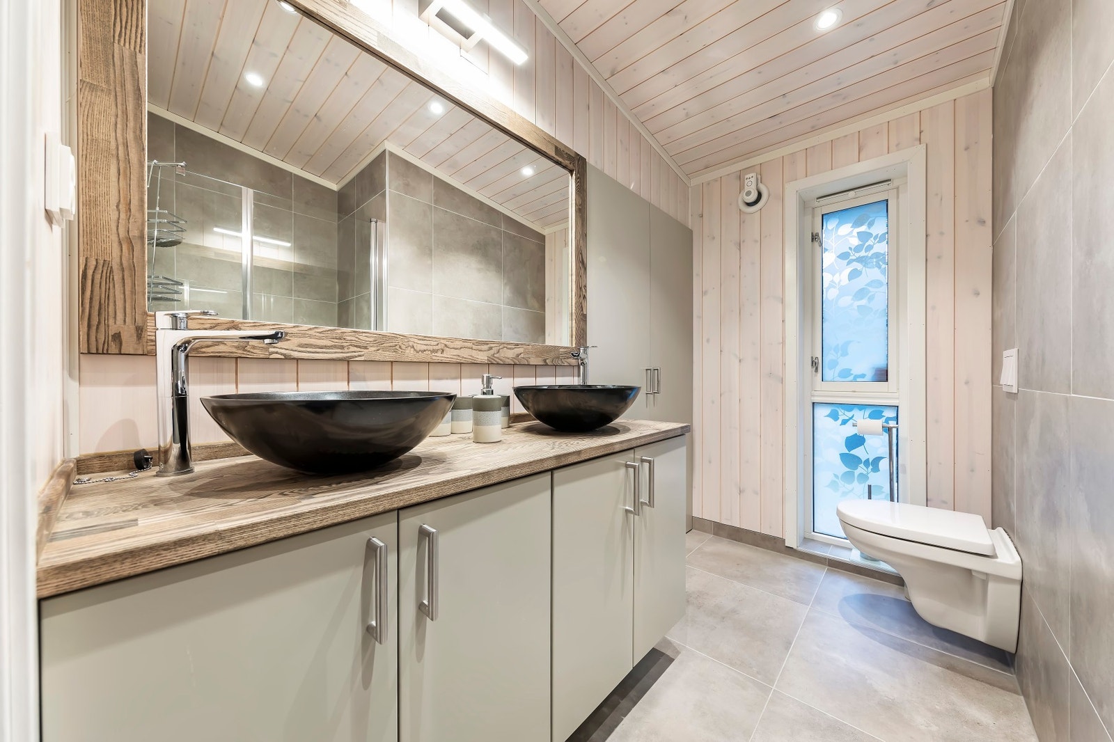 Flislagt bad med dobbelservant, vegghengt toalett og dusjnisje. Bak dørene til høyre finner man et eget rom for vaskemaskin Galleribilde