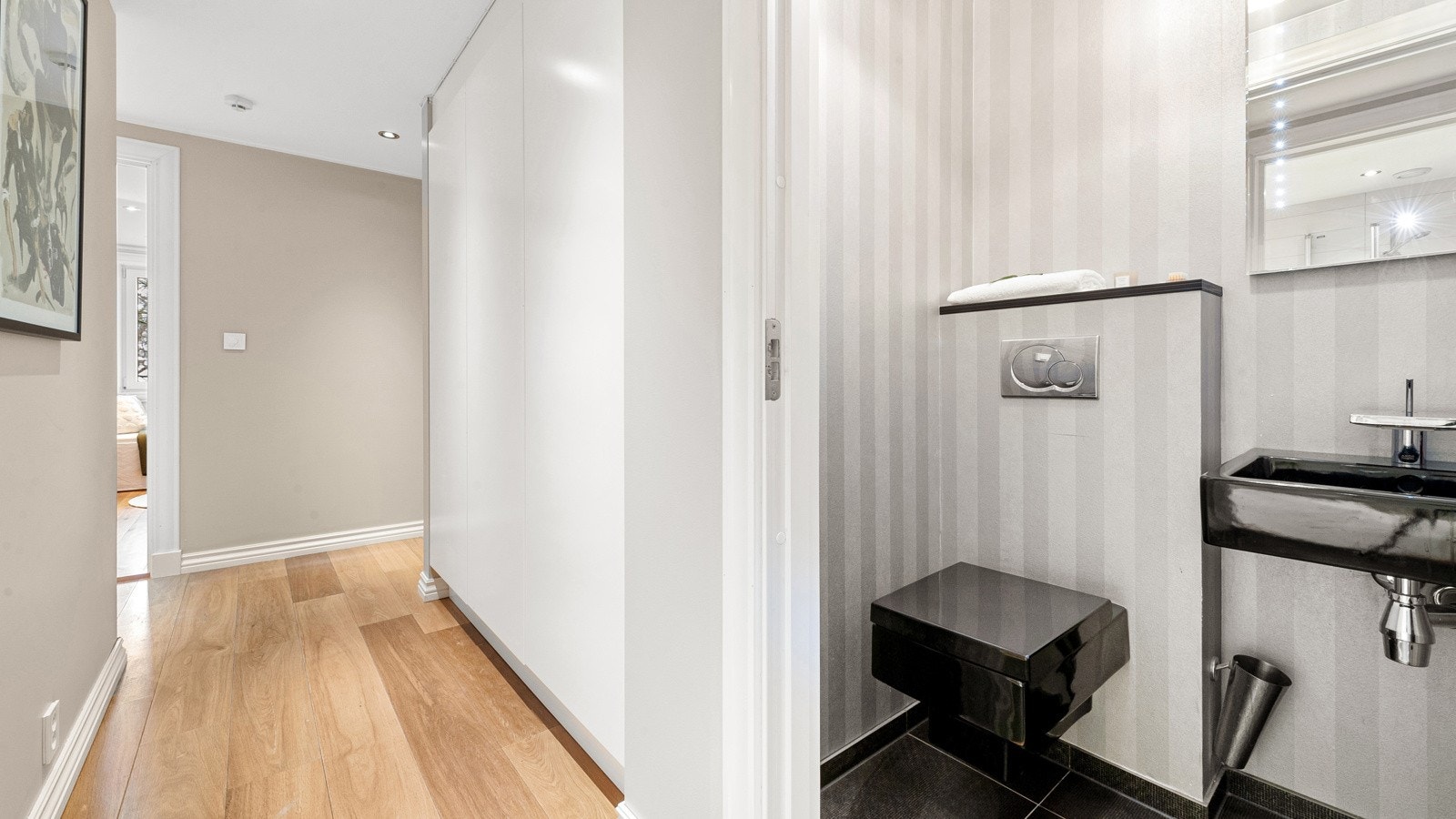 I leiligheten er det to lekre bad, gjestetoalett (avbildet) samt et godt organisert vaskerom. Gjestebad med wc fra Philippe Starck, speil med innebygget lys, designertapet og stilfulle fliser (lik som i yttergang) Galleribilde
