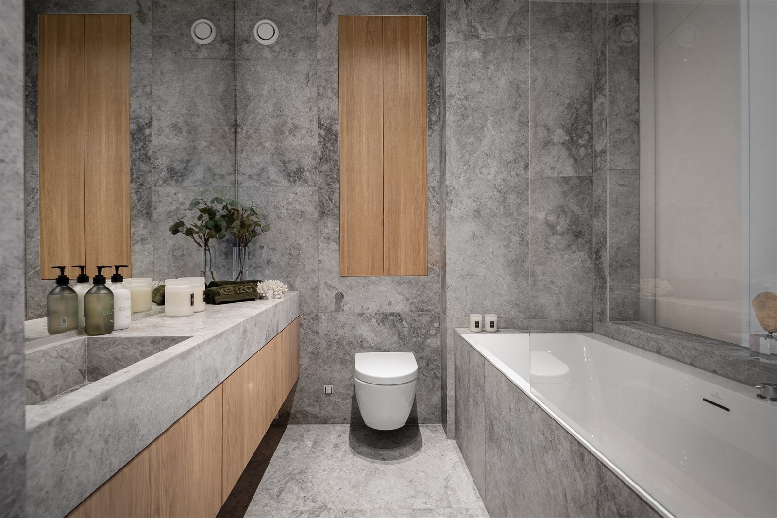 Delikat baderom med store italienske marmorfliser på gulv og vegger. Heldekkende benkeplate med integrert servant i komposittsten og blandebatteri fra Vola samt helt veggspeil over. Galleribilde