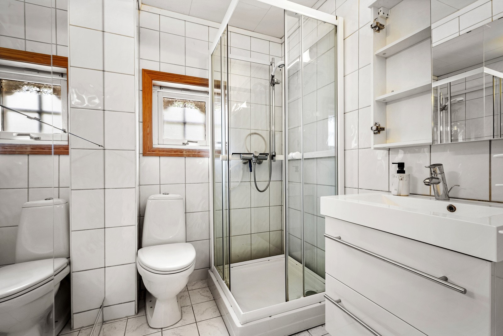Badet i boligen er av flislagte overflater med dusjkabinett og gulvmontert toalett og benkeplate med servant Galleribilde