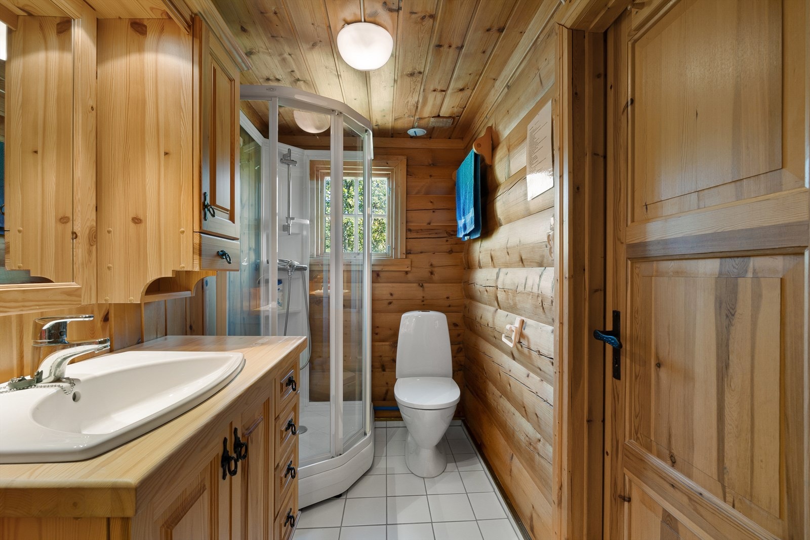 Badet har fliser på gulv med varmekabler og er innredet med servant i møbel, overskap, WC og dusjkabinett. Galleribilde