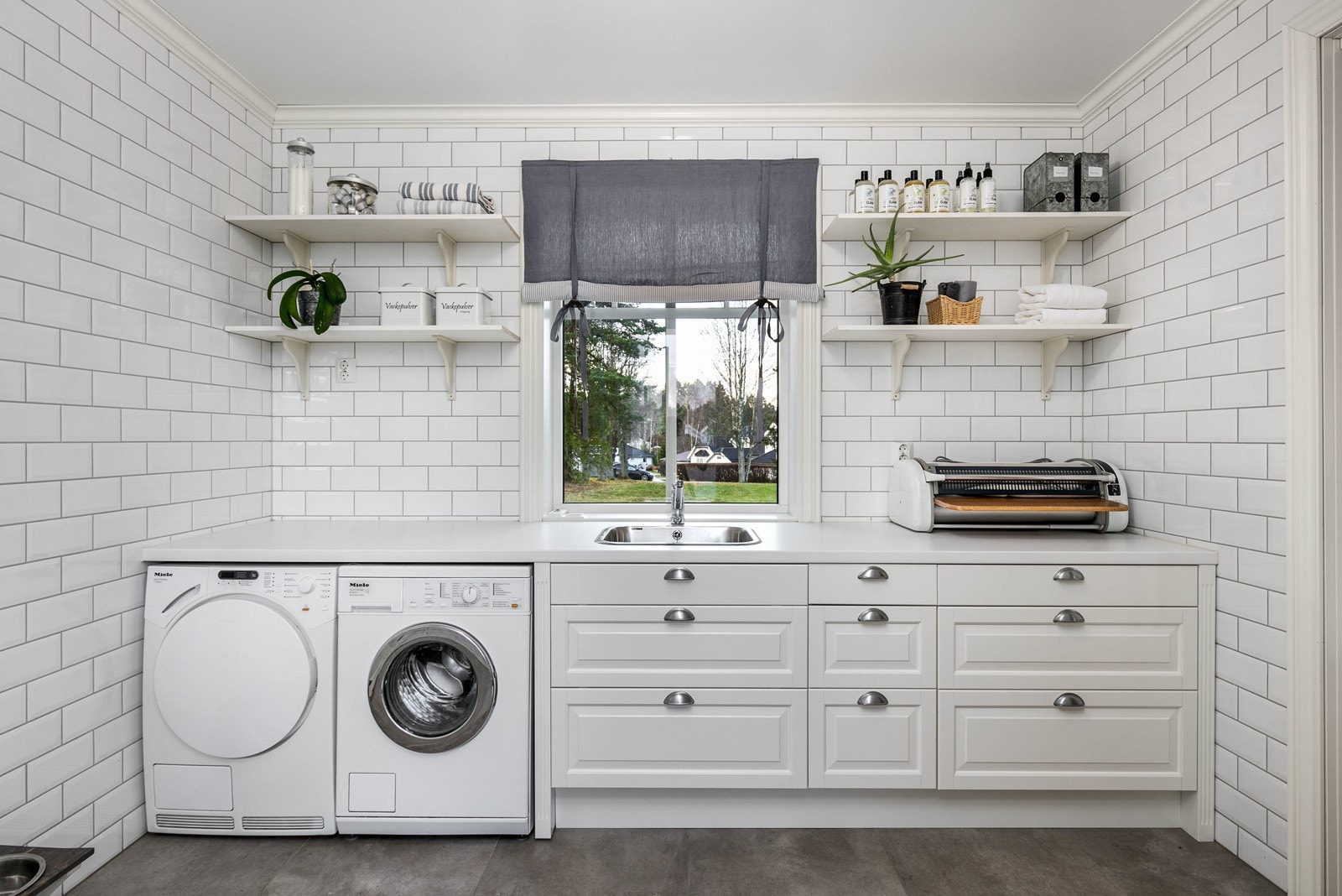 Familievennlig vaskerom i boligens 1. etasje med flislagte overflater og vannbåren varme i gulv. Inneholder bla. plassbygget benkeinnredning fra Epoq m/utslagsvask, div. skuffer, integrert strykebrett, samt opplegg for både vaskemaskin og tørketrommel. Galleribilde