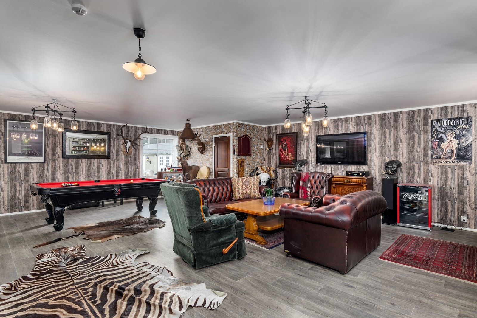 Dagens eier har innredet en hyggelig mancave i opprinnelig del tilhørende garasjerom i 1. etasje. Rommet har platebelagte veggflater og flisimitert belegg på gulv med vannbåren gulvvarme. Galleribilde