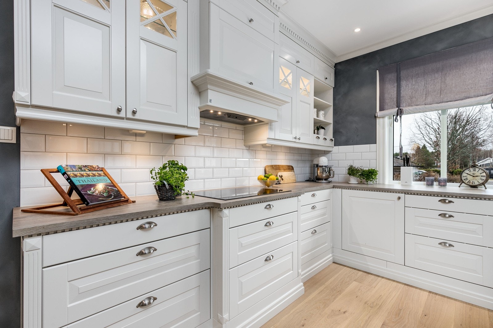 Innredning med hvite profilerte takhøye fronter i kombinasjon med opplyste vitrineskap. Benkeplaten er laminert og med nedfelt dobbel porselensvask og ett-greps blandebatteri. Det er satt inn moderne fliser mellom over- og underskap. Galleribilde