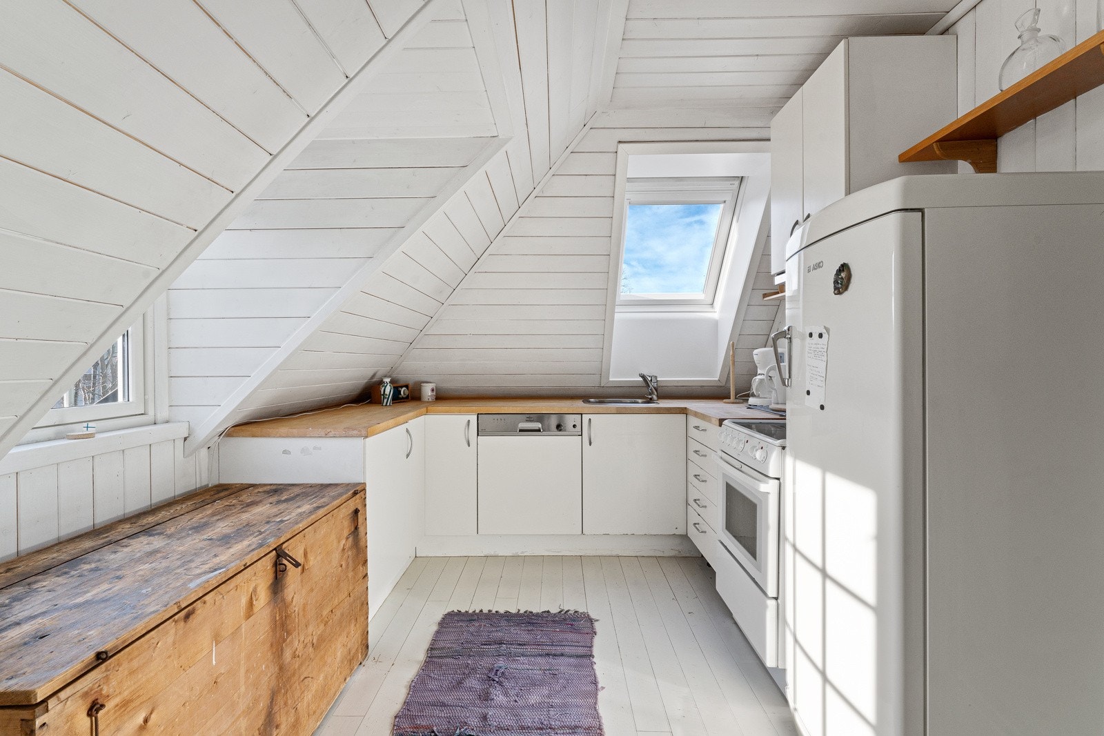 Kjøkkenet i loftsetasjen er luftig og arealeffektivt, og innredningen har hvite fronter, heltre benkeplate og nedfelt kum i stål. Videre er det kullfilterventilator, benkestikk og nisje for frittstående komfyr. Galleribilde