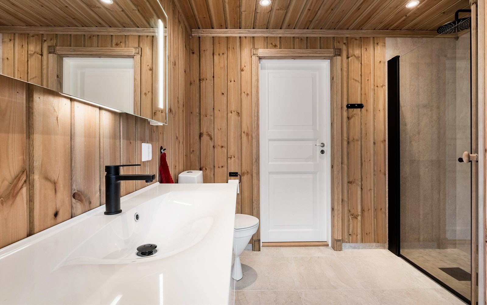 Badet har en romslig dusjnisje, toalett, servantinnredning og overspeil med integrert lys. Galleribilde