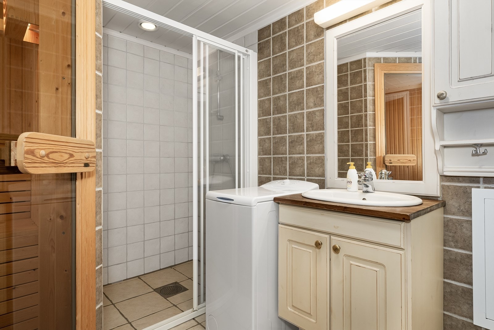 Badet har flislagte overflater, klosett, servant, dusj skyvedør samt opplegg for vaskemaskinen. Galleribilde