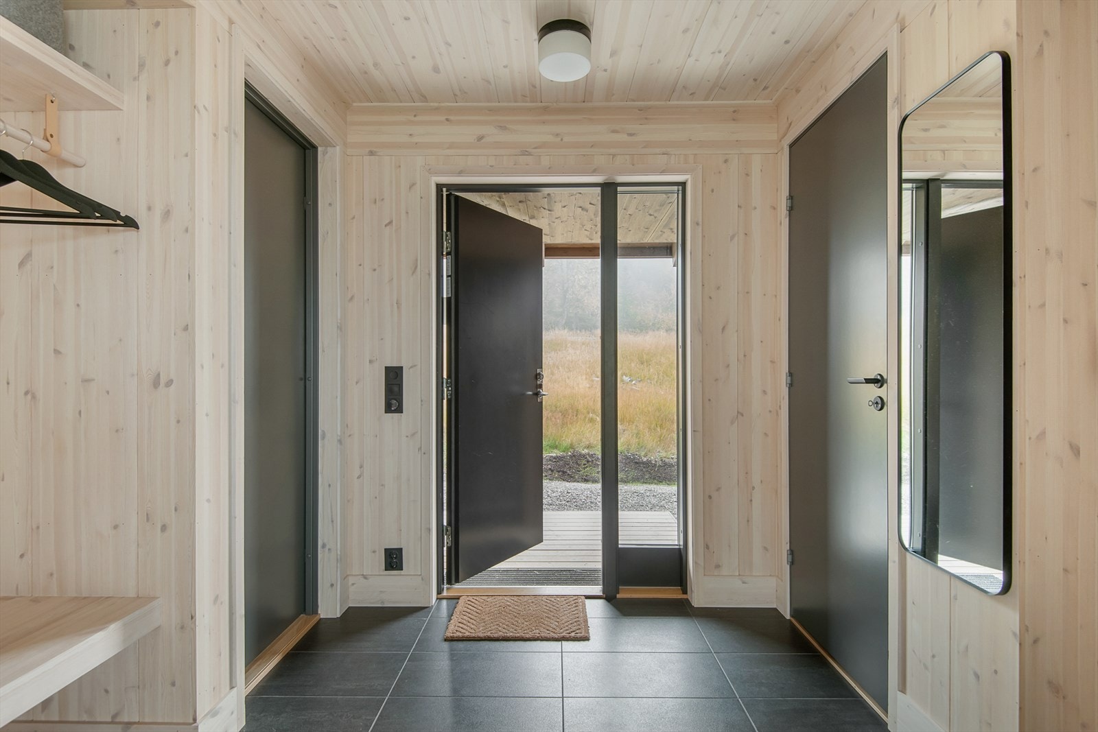 Velkommen inn! Fra overbygget inngangsparti kommer man inn i en praktisk innredet entré med mørke, store fliser på gulv. Galleribilde