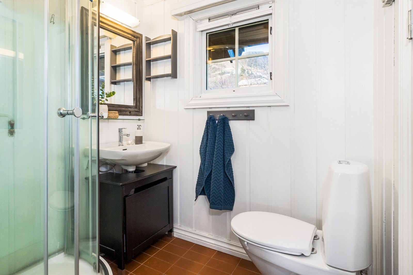 Badet er innredet med fliser på gulv og lysmalt panel på veggene. Galleribilde