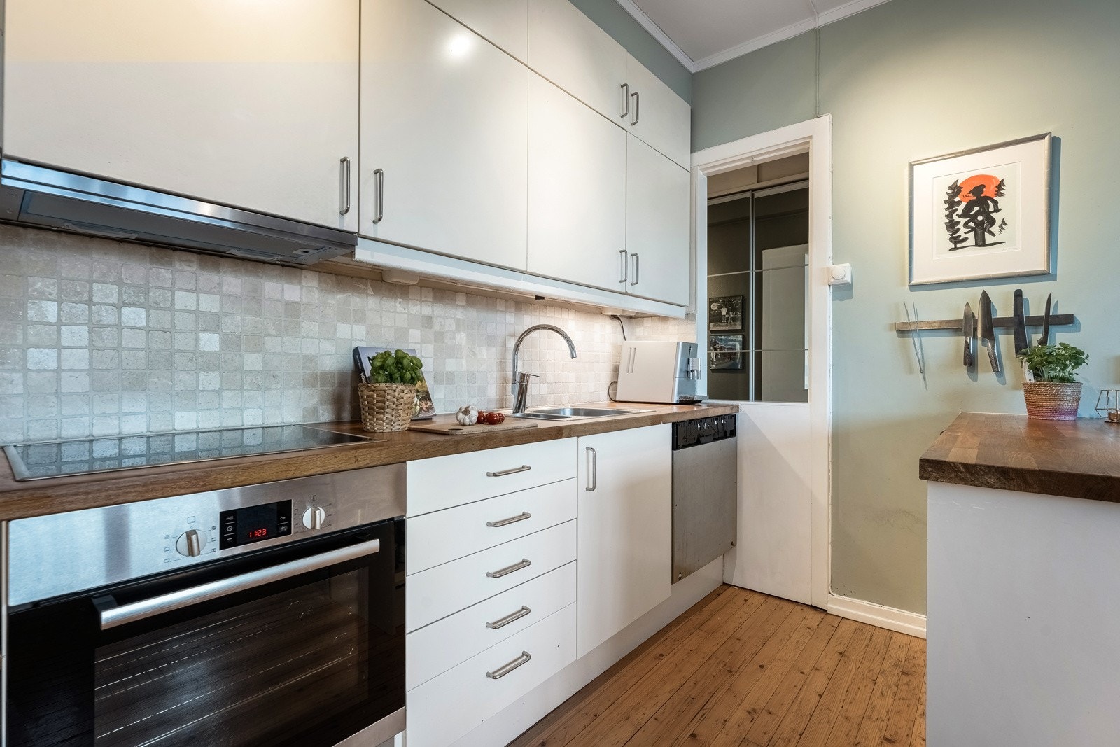 Innredningen har lyse, slette fronter og heltre benkeplate med nedfelt stålkum. Videre har kjøkkenet integrerte hvitevarer som oppvaskmaskin, stekeovn og platetopp fra Bosch, samt to stykk benkekjøleskap fra Siemens Galleribilde