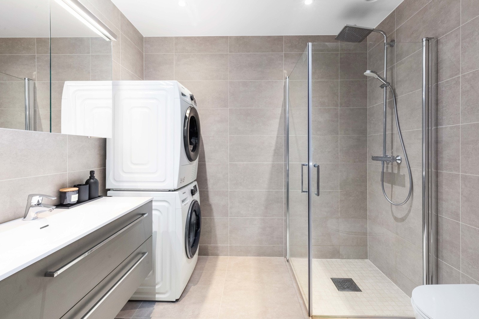 Lekkert flislagt bad med dusjhjørne, vegghengt toalett, dusj med underskuffer og opplegg til vaskemaskin og tørketrommel Galleribilde
