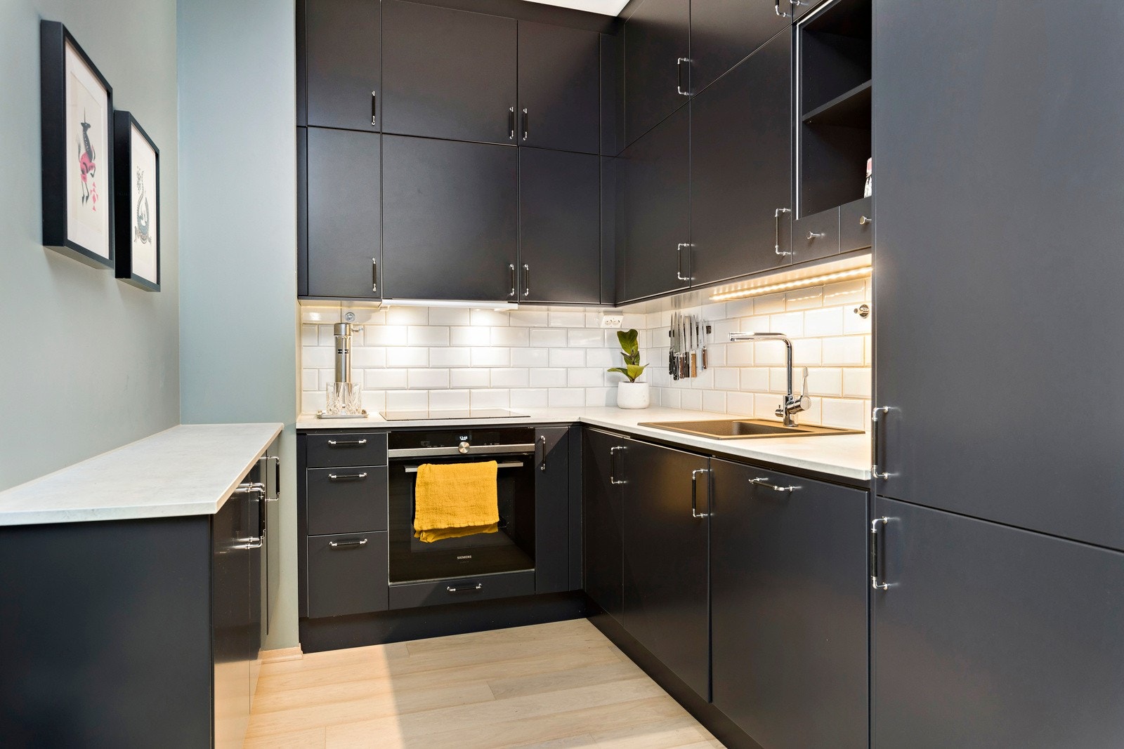 Takhøy kjøkkeninnredning med malte glatte fronter, laminat benkeplater, oppvaskkum, ventilator, fliser over benk, belysning under overskap, integrert oppvaskmaskin, kjøl/fryseskap, stekeovn og induksjon platetopp. Galleribilde